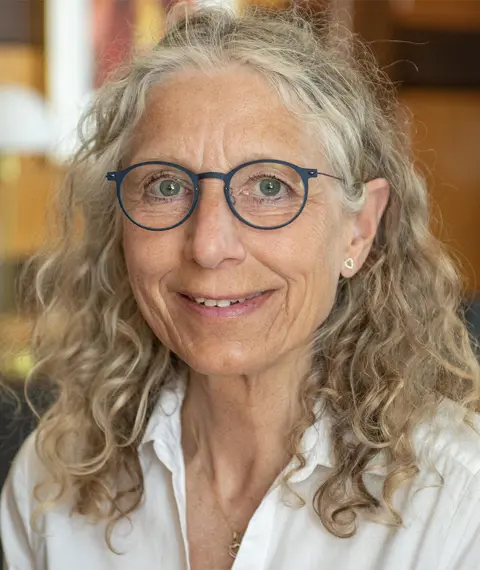 Smilende portræt af kvinde med briller og krøllet gråt hår.