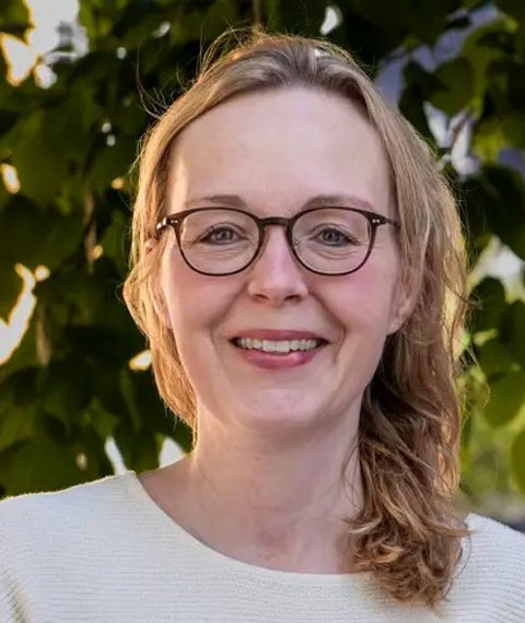 Smilende portræt af kvinde med briller foran grønne blade.