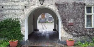 Buet murstensindgang til klostergård med potteplanter.