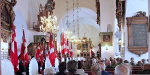 Kirkerum fyldt med menighed og danske flag til gudstjeneste.